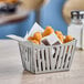 A Tablecraft stainless steel side French fry basket filled with fried chicken nuggets on a table.