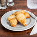 A Carlisle smoke melamine bread and butter plate with two croissants on it.