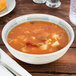 A Carlisle smoke melamine bowl of soup with vegetables and bread on a table.