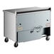 A True worktop refrigerator with a stainless steel counter top on a metal box with wheels.