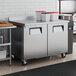 A stainless steel worktop freezer with two doors, a backsplash, and casters, situated in a commercial kitchen.