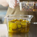 A person holding a Turbo Air clear plastic food pan filled with pickles.