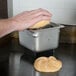 A person using a Prince Castle stainless steel butter spreader to butter a piece of bread.