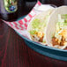 A table with a plate of tacos served in a blueberry oval deli server.