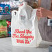 A person holding a white plastic t-shirt bag with red "Thank You" text.