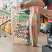 A man putting a plastic bottle into a beige Choice heavy-duty plastic bag with "Thank You" on it.