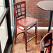 A Lancaster Table & Seating mahogany wood bar stool with a mahogany wood seat next to a table in a restaurant dining area.