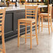 A row of Lancaster Table & Seating wooden bar stools with natural wood seats next to a counter.