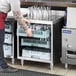 A person in a black shirt putting glasses in a Regency glass rack on a counter.