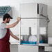 A commercial tall door type dishwasher with a blue dish rack and white plates being loaded by a person.