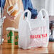 A person holding a white plastic bag with red text that says "Thank You" containing food.