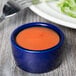 A blue Tuxton pipkin ramekin filled with orange liquid on a table with a blurry fork.