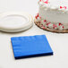 A white cake with red sprinkles next to a stack of blue Creative Converting beverage napkins.