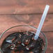 A glass with a straw in it on a brown liquid.