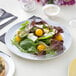 A Visions white plastic plate with a salad of tomatoes and greens.