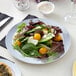 A Visions white plastic plate with salad, tomatoes, and cheese.