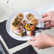 A person holding a Visions white plastic plate with food on a table.