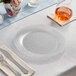 A Visions clear plastic plate with silverware on a table.