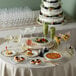 A table with Visions disposable plastic bowls filled with food and a cake with fruit on top.