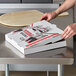 A person opening a Choice white corrugated pizza box on a table.