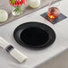 A Visions black plastic plate on a table with silverware and a napkin.