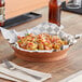 A terracotta round plastic fast food basket filled with food on a table.