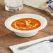 A Visions ivory plastic bowl filled with soup on a table with a silver spoon.