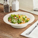 A Visions Wave ivory plastic bowl filled with salad with cucumbers and carrots on a table.