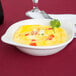 A white Tuxton round china dish with a shirred egg inside garnished with tomatoes and parsley.