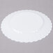 A white Fineline Flairware plastic plate with scalloped edges on a white surface.