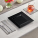 A Visions Florence black square plastic plate on a white surface with a fork and knife.