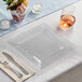 A clear Visions Florence square plastic plate with silverware on a table with flowers.