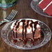 A clear plastic plate with a slice of chocolate cake and chocolate sauce with a fork.