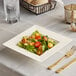 A Visions Florence ivory square plastic bowl filled with salad on a table with a fork and knife.