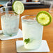 Two Choice clear plastic tumblers of water with ice and lime slices on a table.