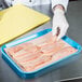 A person in gloves holding a tray with raw chicken breasts on a pink LitePeachTreat steak paper sheet.