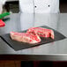 A chef cutting raw meat on a black surface using Choice black steak paper.