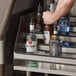 A man pouring vodka into a bottle on a Regency stainless steel liquor display shelf.