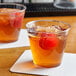 A pair of Choice clear plastic tumblers filled with ice and liquid, each garnished with a cherry.