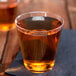 A close-up of a Choice clear plastic shot glass filled with brown liquid.