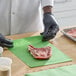 A person wearing black gloves is placing a raw steak on a green 9" x 12" steak paper sheet.
