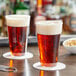 Two Choice clear plastic tumblers filled with beer on a table.