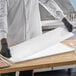 A stack of white 10" x 30" steak paper sheets being handled by a person wearing black gloves in a food preparation area.