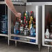 A man's arm placing a bottle of alcohol into a Regency stainless steel liquor display cabinet.