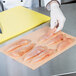 A person using LitePeachTreat steak paper to wrap raw chicken breasts on a cutting board.