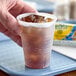 A hand holding a Dart translucent plastic cold cup with ice in it.