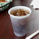 A Dart Y9 Conex translucent plastic cup with a drink and a straw on a table.