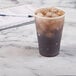 A Dart Conex translucent plastic cup filled with iced coffee on a table with a notebook and pen.