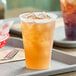 A Dart Conex translucent plastic cup filled with ice and orange liquid on a tray.