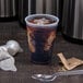 A Dart translucent plastic cup with brown liquid and ice on a counter.